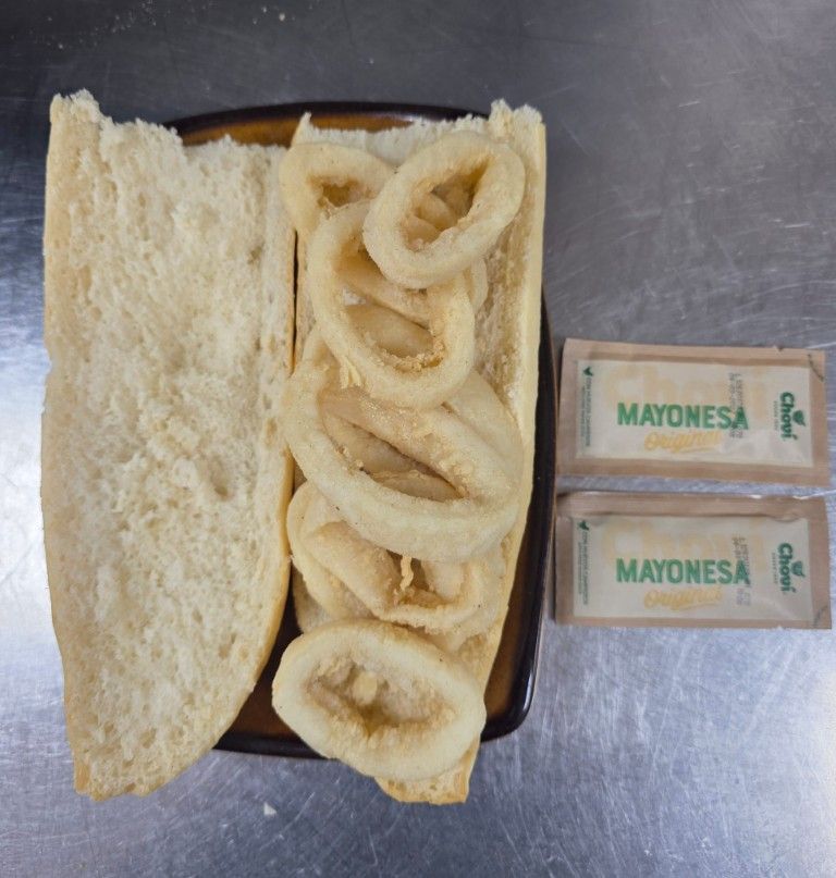 Sándwich con aros de huevo y dos paquetes de mayonesa en una bandeja
