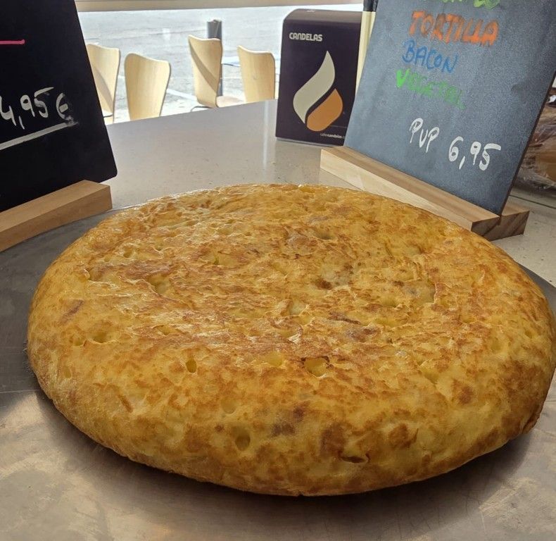 Una gran tortilla redonda de color marrón dorado sobre un mostrador, con pequeños letreros con el menú detrás.