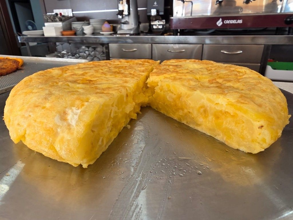 Tortilla dorada hecha en una plancha de metal, cortada por la mitad en una cocina.