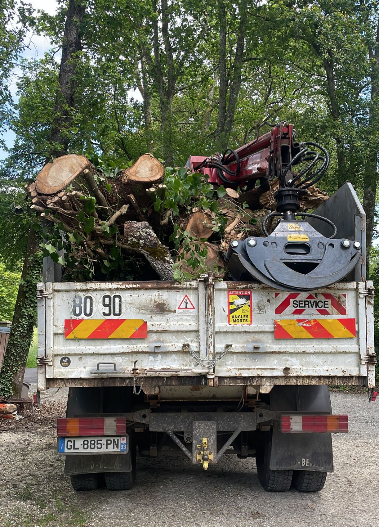 Un camion chargé de troncs d'arbres coupés et une grue sont stationnés sur une route forestière.