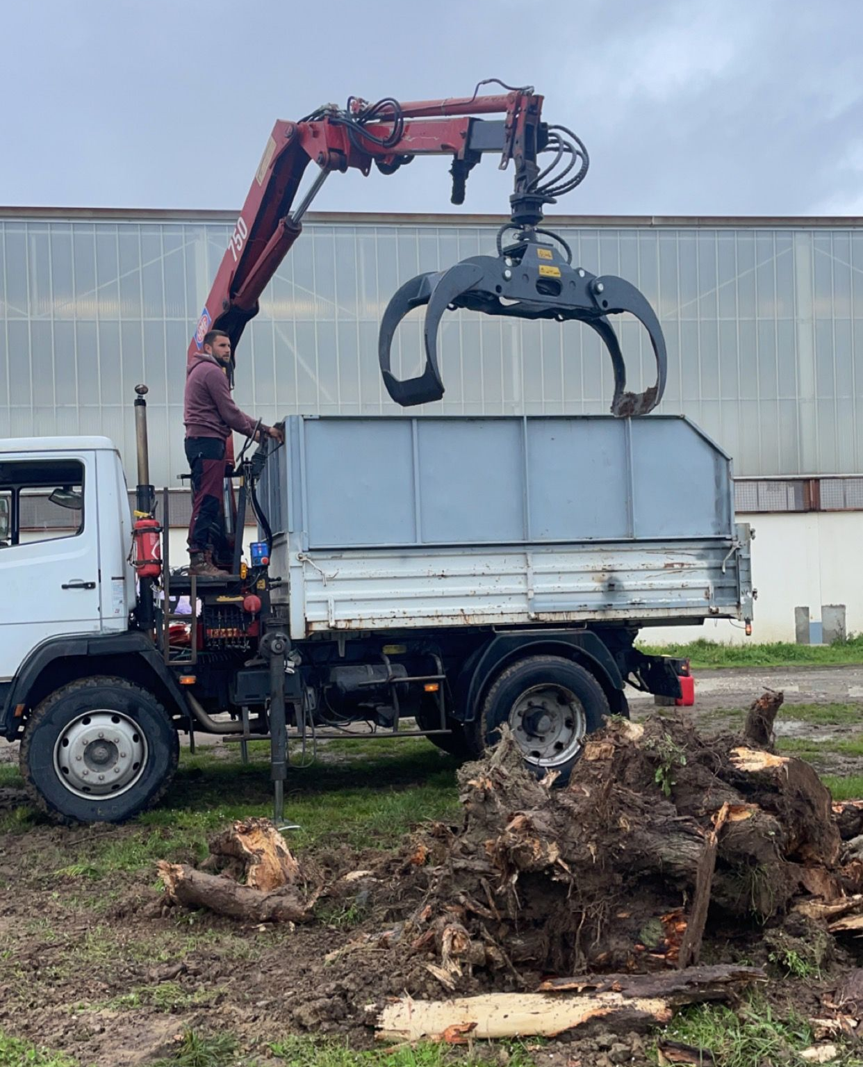 Camion-grue soulevant un grand conteneur métallique à côté d'une pile de bûches coupées à l'extérieur