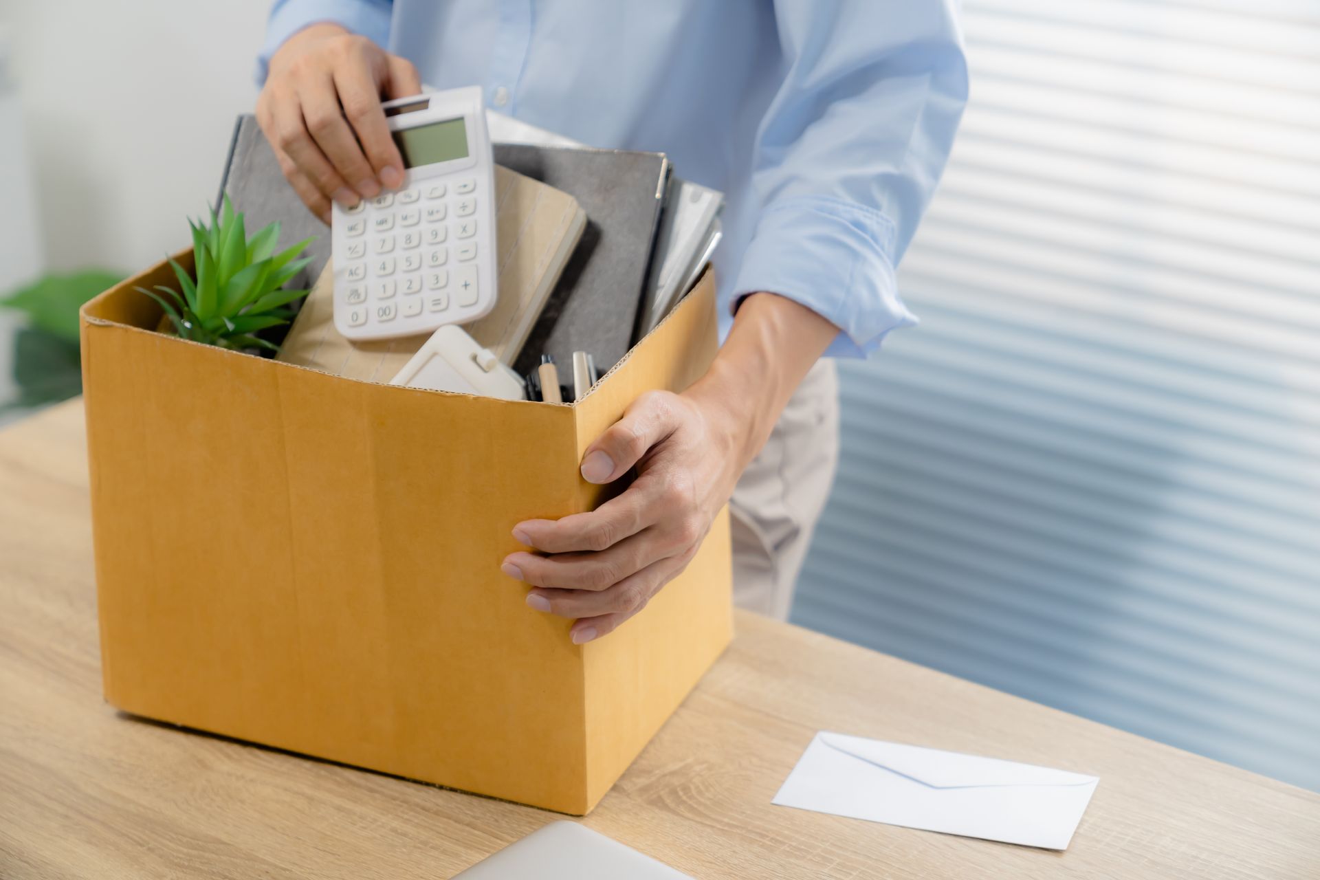 Photo de quelqu'un qui porte un carton plein d'affaires de bureau, avec une lettre à côté.