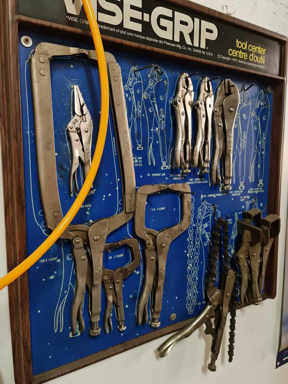 Ein Bündel Zangen hängt an einer Wand unter einem Schild mit der Aufschrift „Schraubstockgriff“