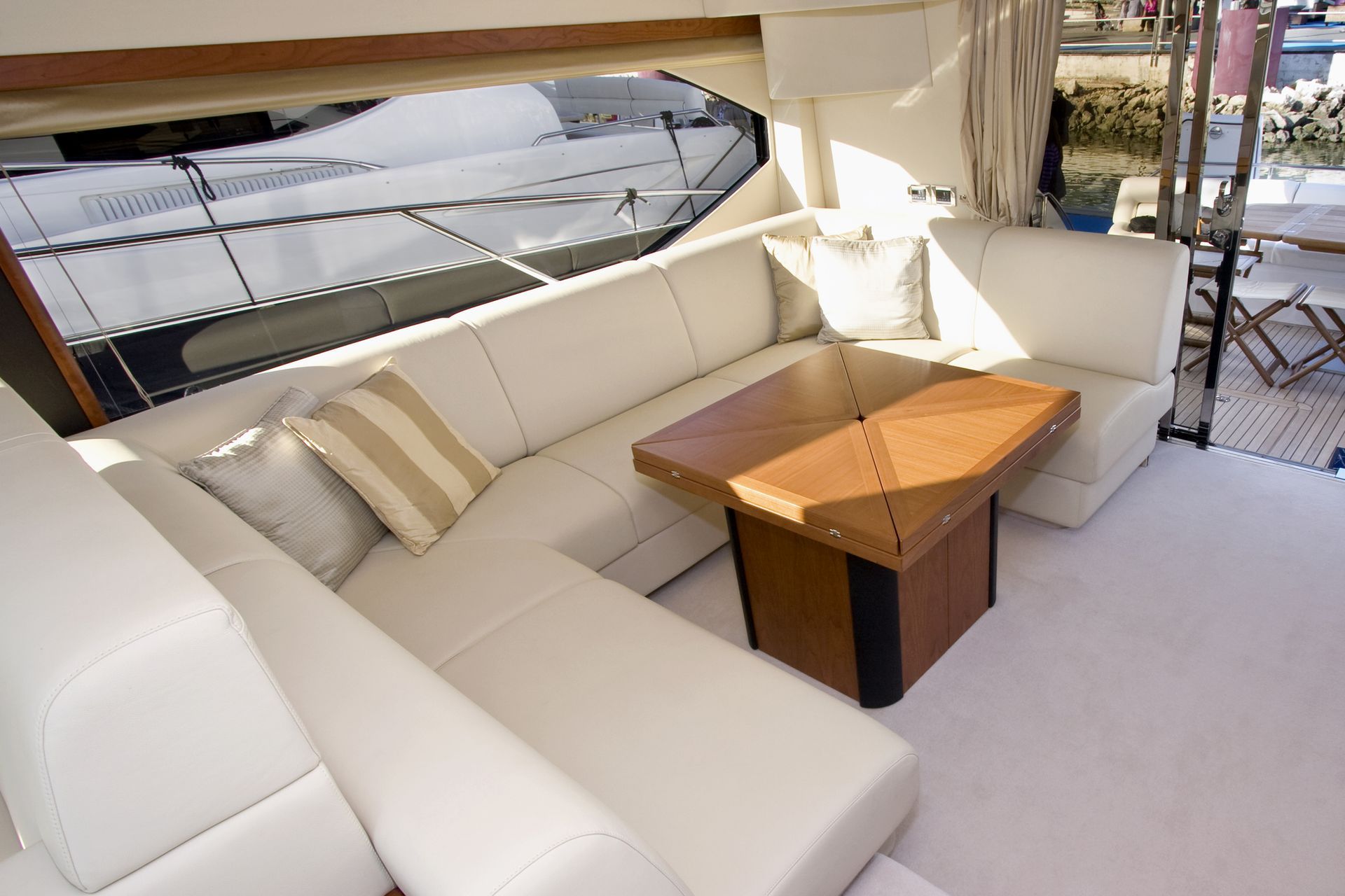 Λευκό δερμάτινο καθιστικό με ξύλινο τραπέζι σε γιοτ, δίπλα σε μεγάλο παράθυρο.