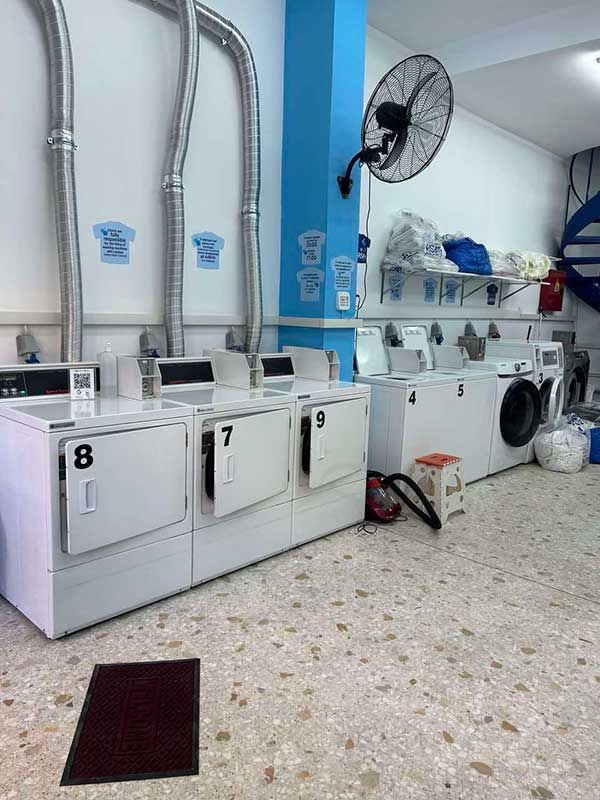 Ένα πλυντήριο με πολλά πλυντήρια και στεγνωτήρια και έναν ανεμιστήρα στον τοίχο.