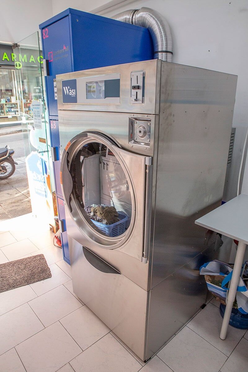 Ένα μεγάλο πλυντήριο ρούχων από ανοξείδωτο ατσάλι βρίσκεται σε ένα δωμάτιο δίπλα σε ένα τραπέζι.