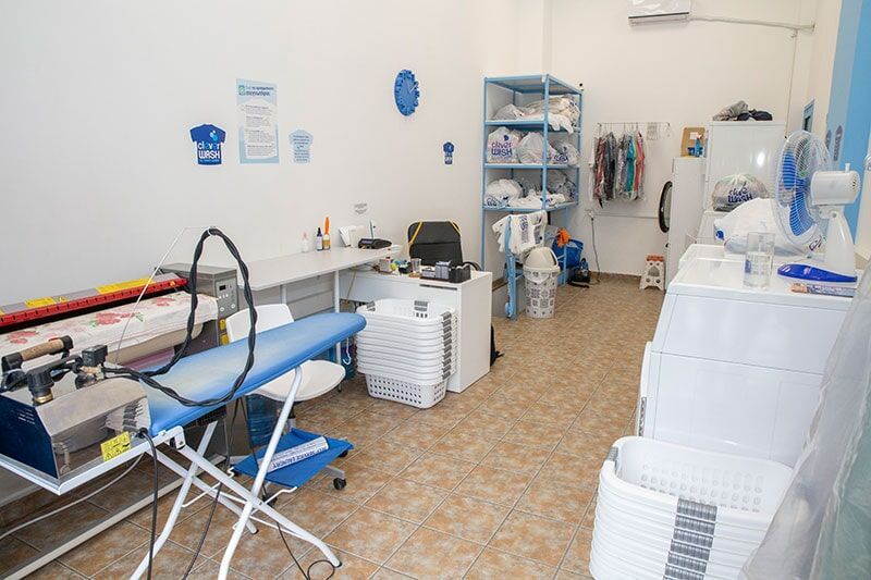 Ένα δωμάτιο πλυντηρίων με πλυντήριο ρούχων, σιδερώστρα και καλάθια.