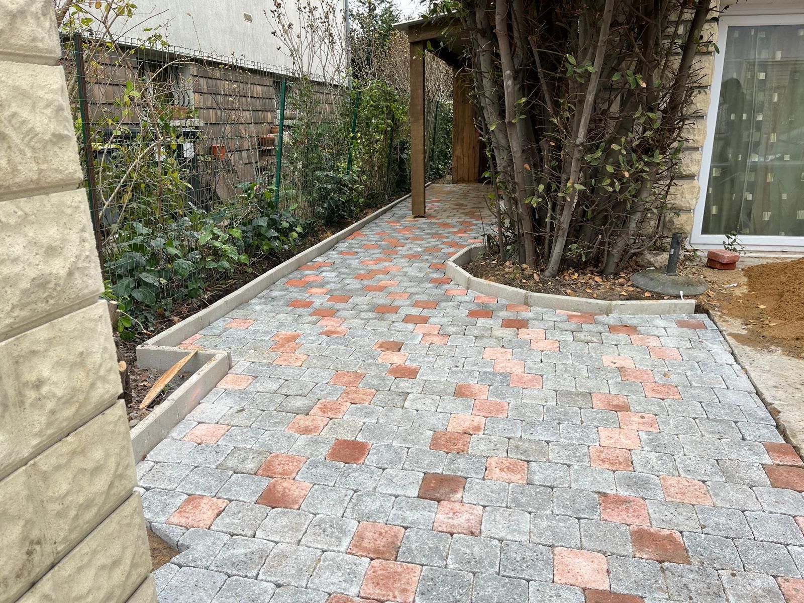 Allée de jardin sinueuse en briques et gravier longeant un grand arbre et un mur blanc