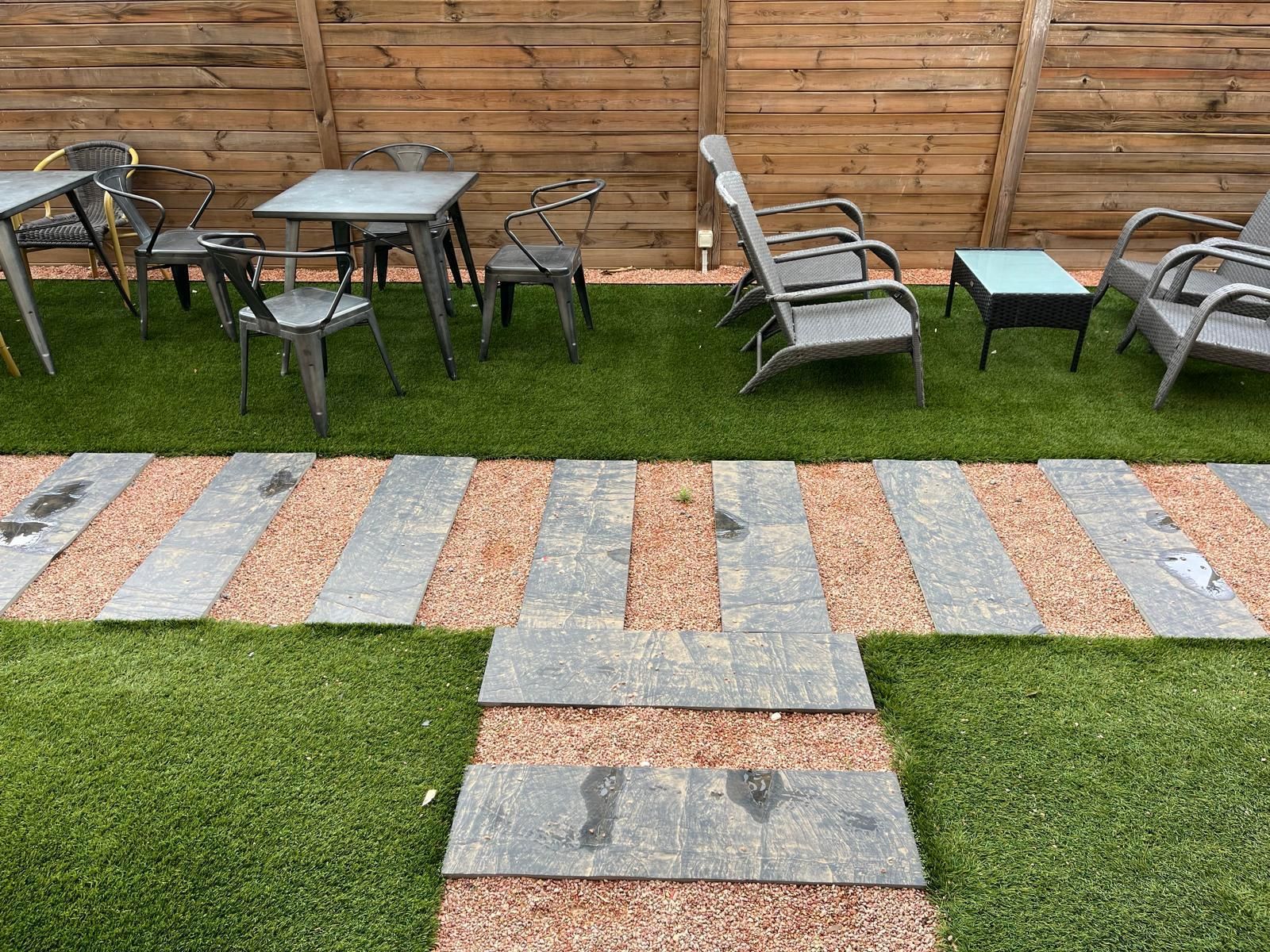 Terrasse arrière avec chaises en métal, table et un chemin de pierres et d'herbe menant à une clôture en bois.