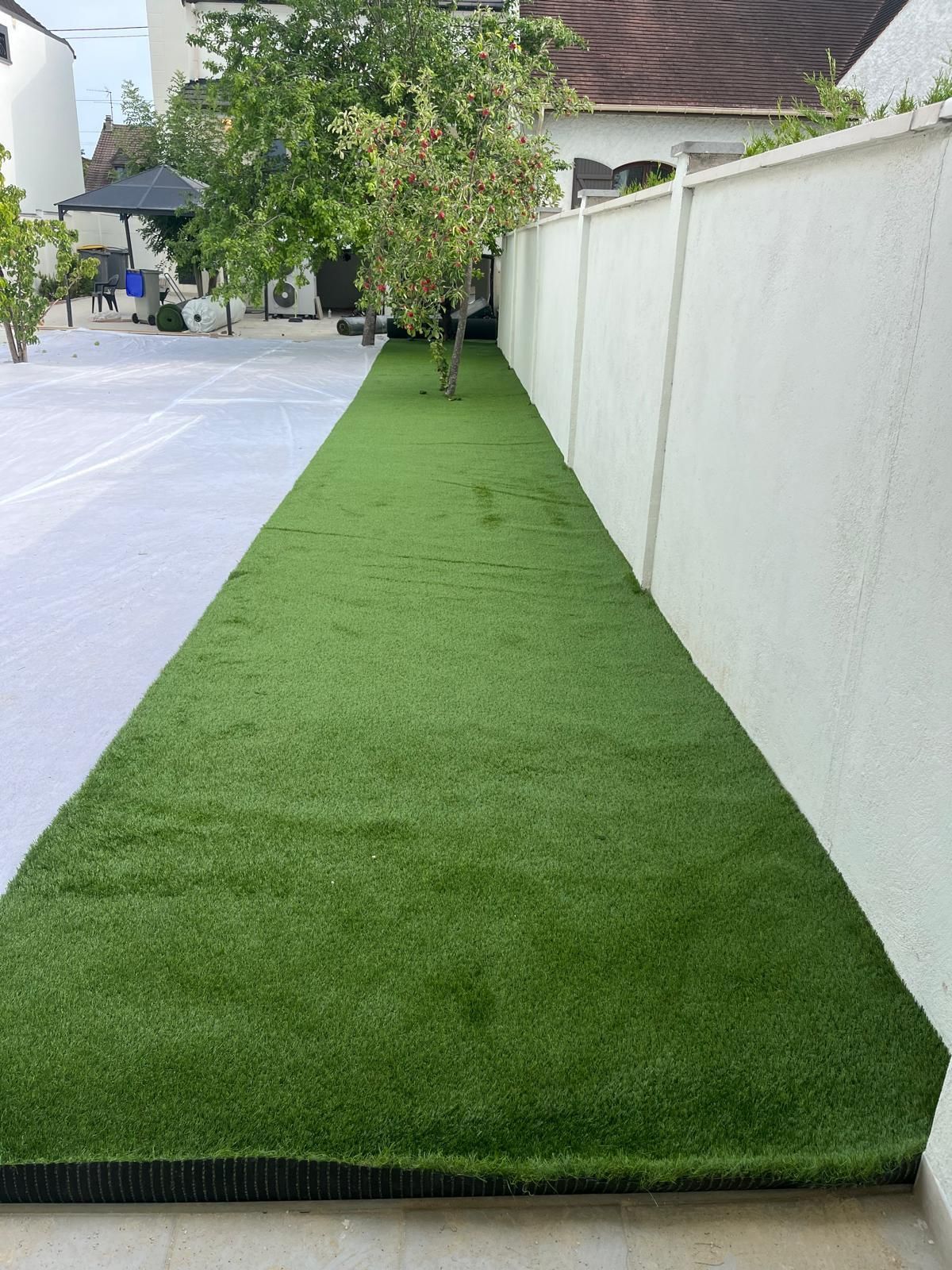 Une étroite bande de gazon artificiel vert longe une clôture blanche et une terrasse.