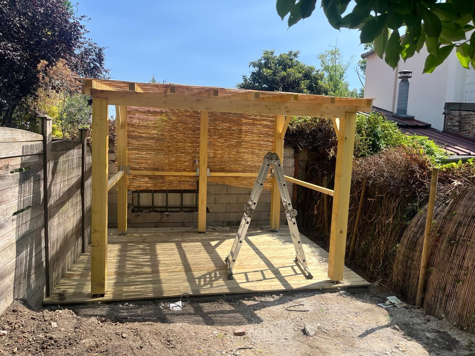 Structure d'abri de jardin en bois avec panneaux muraux en bambou et échelle sur une terrasse pavée