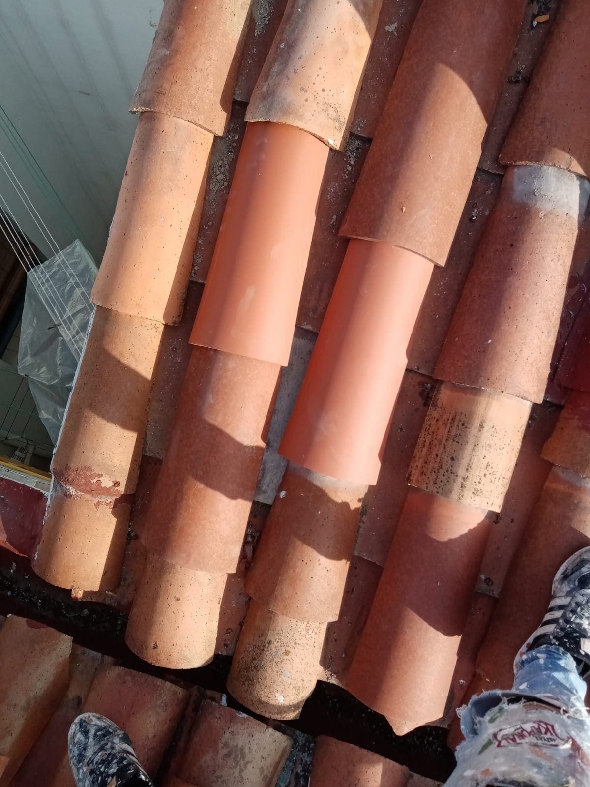 Una persona está parada sobre un tejado con un montón de tejas apiladas una encima de otra.