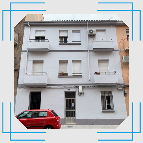 Un coche rojo está aparcado delante de un edificio blanco.
