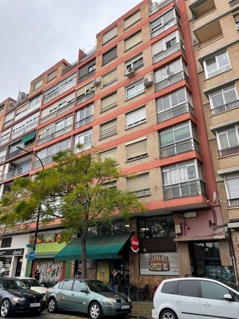 Un edificio con muchas ventanas y coches aparcados delante.