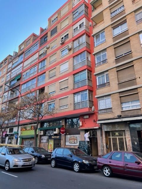 Una fila de coches están aparcados delante de un edificio alto.