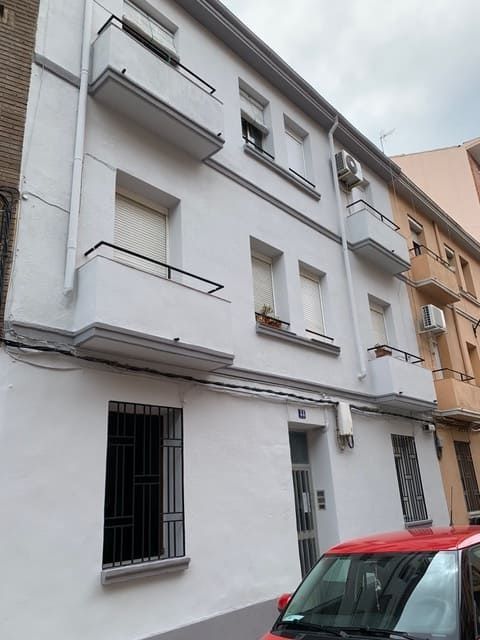 Un coche rojo está aparcado delante de un edificio blanco.