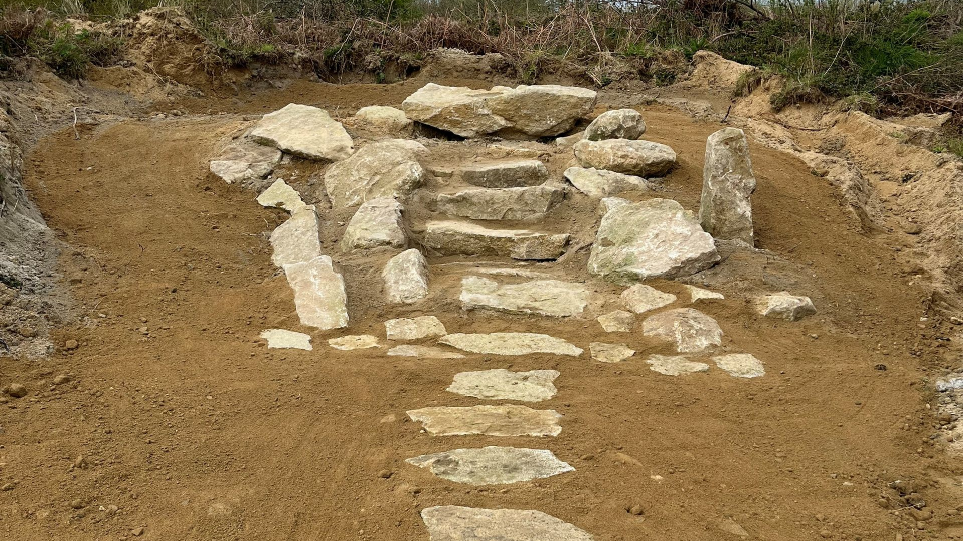 Fosse d'excavation revêtue de pierres dans un sol sec, avec un petit amas central de pierres et des parois de terre.