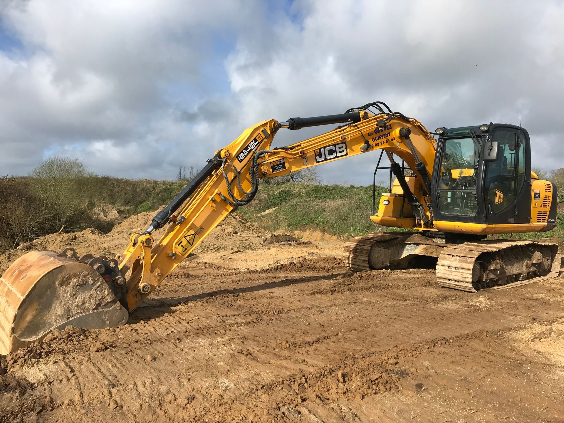Une pelleteuse jaune creuse la terre sur un chantier de construction sous un ciel nuageux.