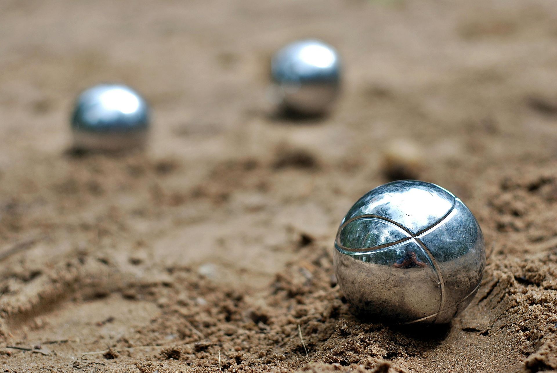 Trois boules de pétanque métalliques sur un terrain en terre battue, l'une d'elles, très nette, au premier plan.