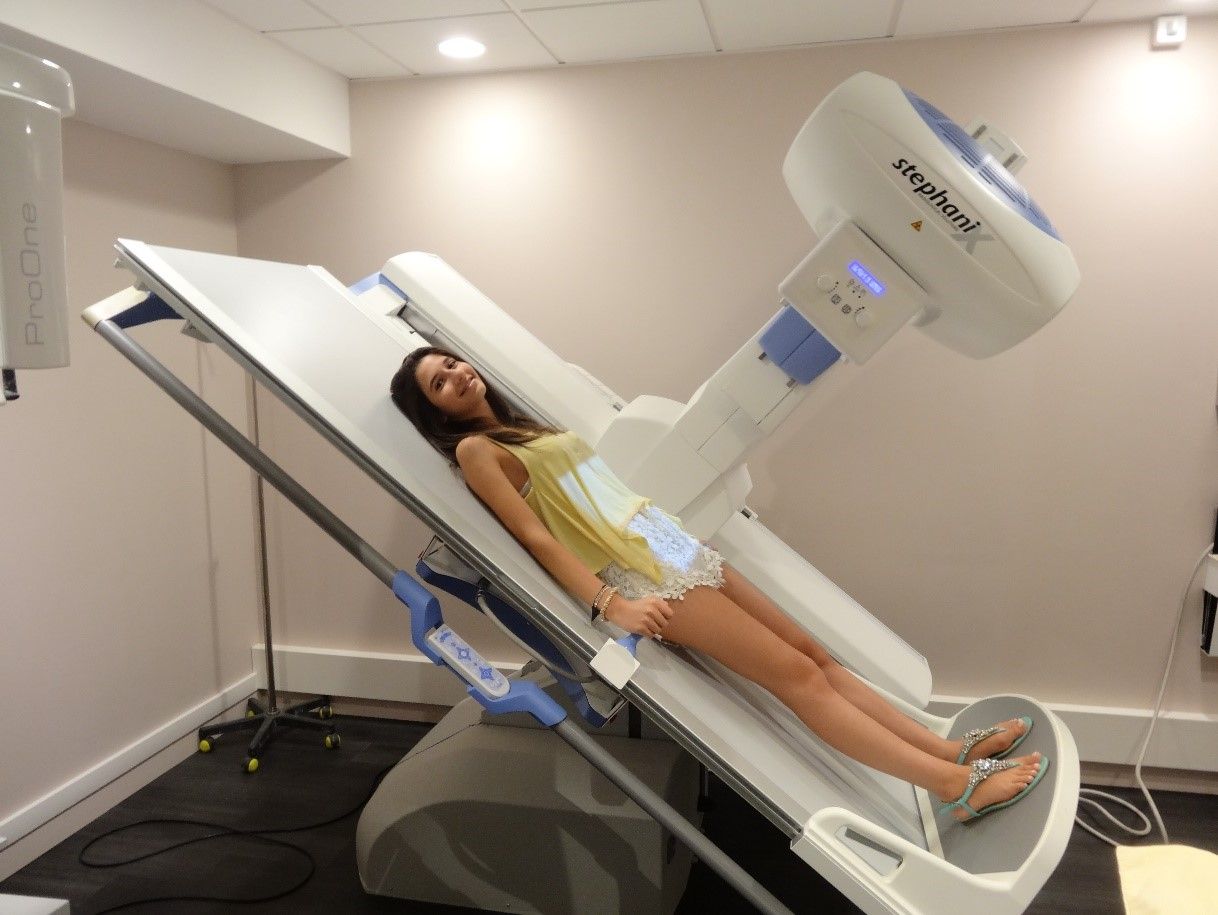 Patient allongé sur une table d'imagerie médicale inclinée, à côté d'un grand scanner, dans une salle de consultation.