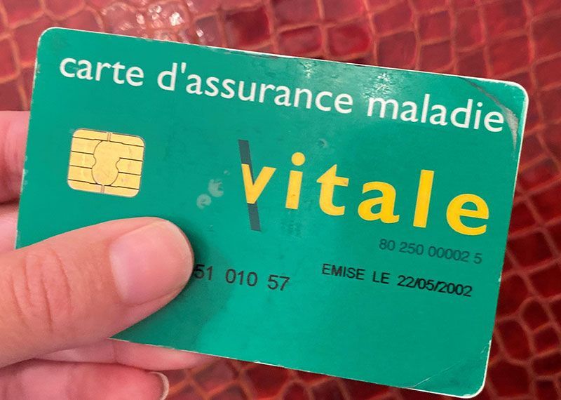 Main tenant une carte d'assurance maladie Vitale verte sur fond rouge