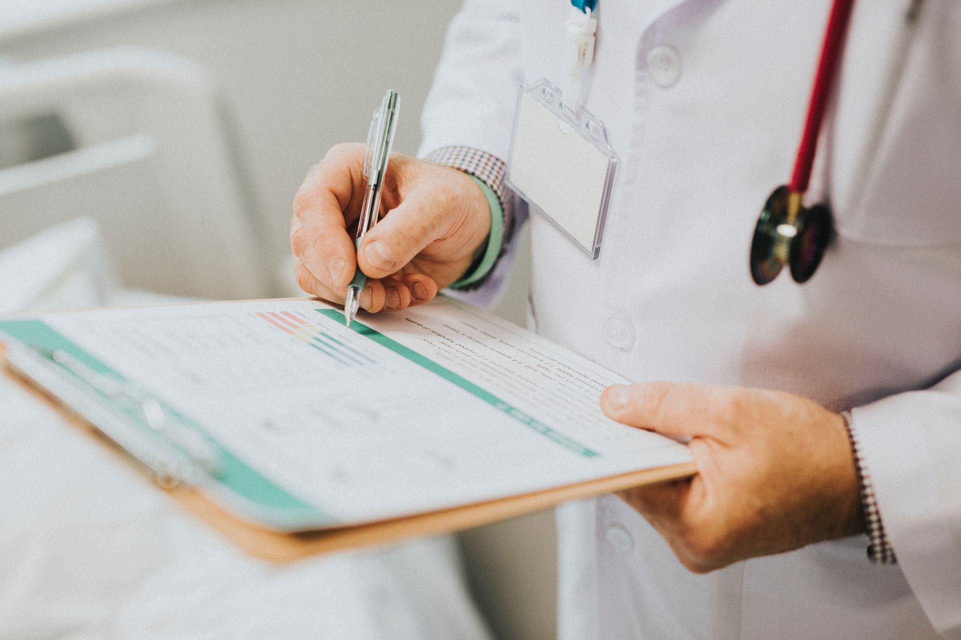 Un médecin écrivant sur un bloc-notes avec un stylo, portant une blouse blanche et un stéthoscope.