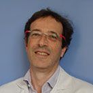Un homme portant des lunettes et une chemise blanche sourit sur un fond bleu.
