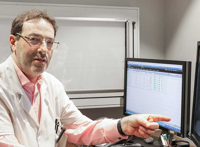 Un homme en blouse blanche désigne un écran d'ordinateur dans un laboratoire ou un bureau.