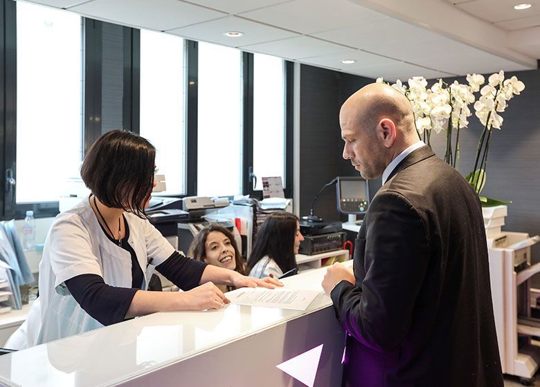 Un employé assiste un client au comptoir du service clientèle dans le hall d'un immeuble de bureaux moderne.