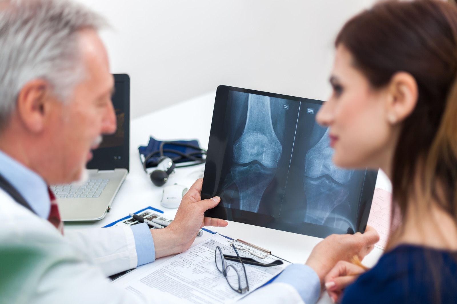 Un médecin et un patient examinent une radiographie du genou sur un ordinateur portable dans le cabinet d'une clinique.