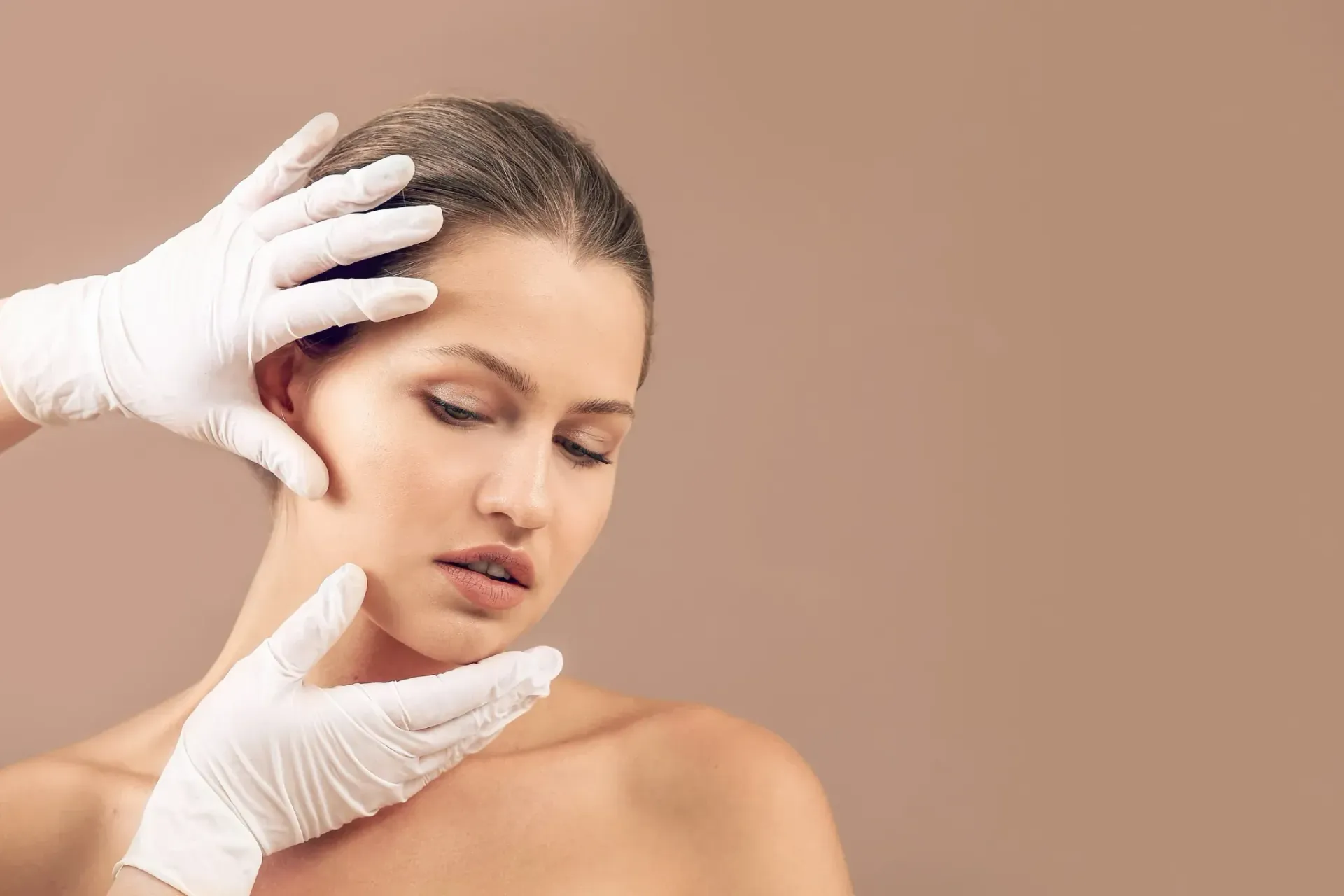 Mujer con manos enguantadas de color blanco cerca de su cara, posiblemente con el pelo teñido, sobre un fondo beige.