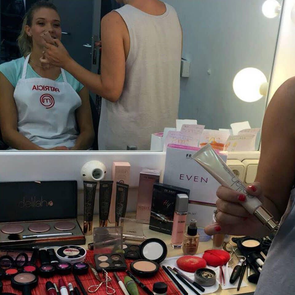 Mujer con delantal a la que le están aplicando maquillaje en un tocador con diversos cosméticos.