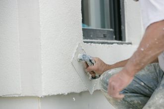 Personne appliquant du crépis avec une truelle sur un mur extérieur près d'une fenêtre.