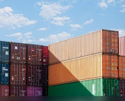 Des conteneurs maritimes empilés, de couleur bordeaux, beige, orange et verte, sous un ciel bleu.