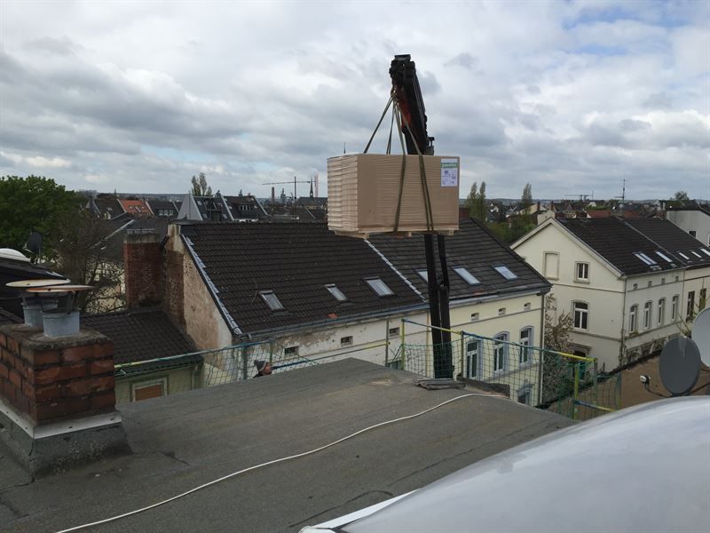 Eine Kiste wird von einem Kran auf ein Dach gehoben.