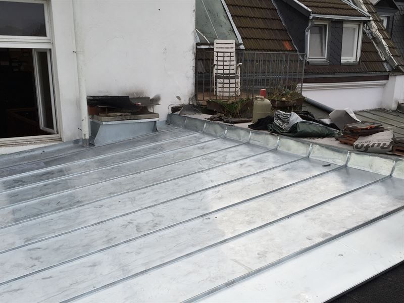 Auf einem Gebäude befindet sich neben einem Fenster ein Metalldach.