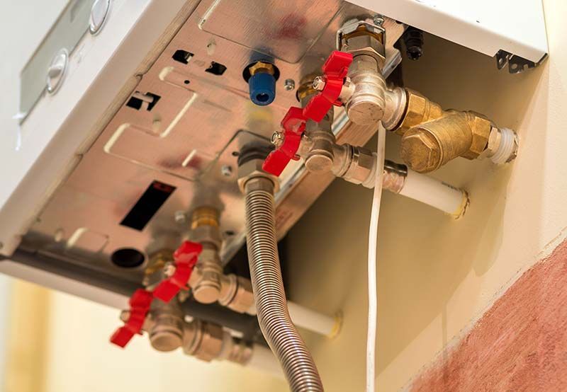 Gros plan des tuyaux et des vannes d'une chaudière avec des poignées rouges et bleues, montées sur un mur beige.