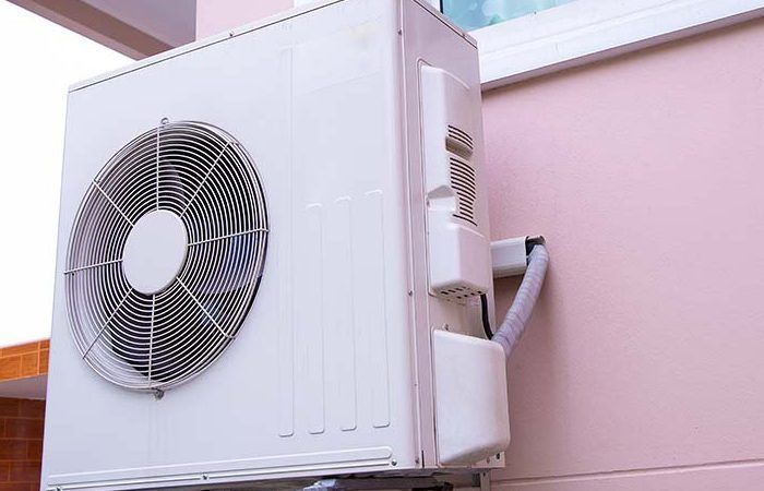 Unité de climatisation blanche montée sur un mur extérieur rose.