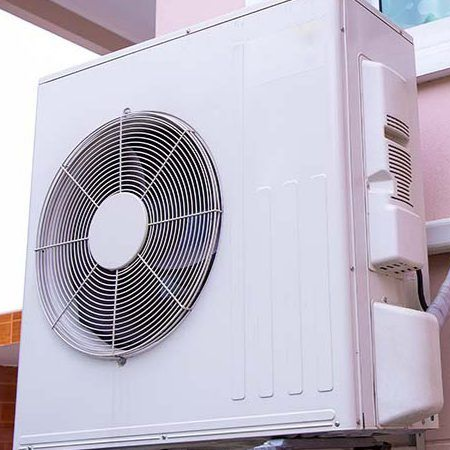 Un homme en salopette bleue installe un chauffe-eau solaire sur un toit sous un ciel bleu.