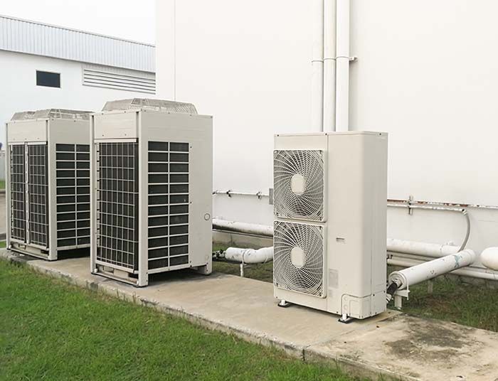 Trois unités de climatisation industrielles à côté d'un bâtiment sur une dalle de béton.