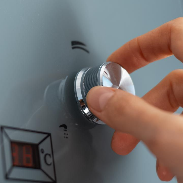 Une main tourne un bouton argenté sur un appareil gris doté d'un affichage numérique indiquant la température en degrés Celsius.