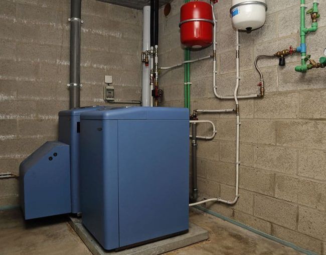 Équipement de système de chauffage bleu dans un sous-sol avec réservoirs d'eau rouges et blancs.