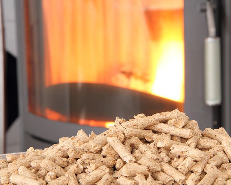 Tas de granulés de bois devant une cheminée allumée, avec des flammes visibles.