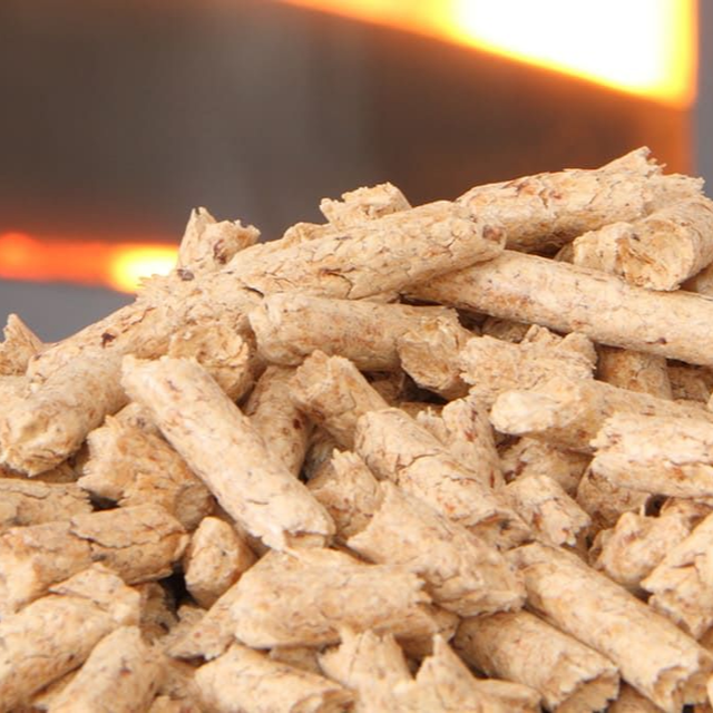 Tas de granulés de bois avec un feu flou en arrière-plan.