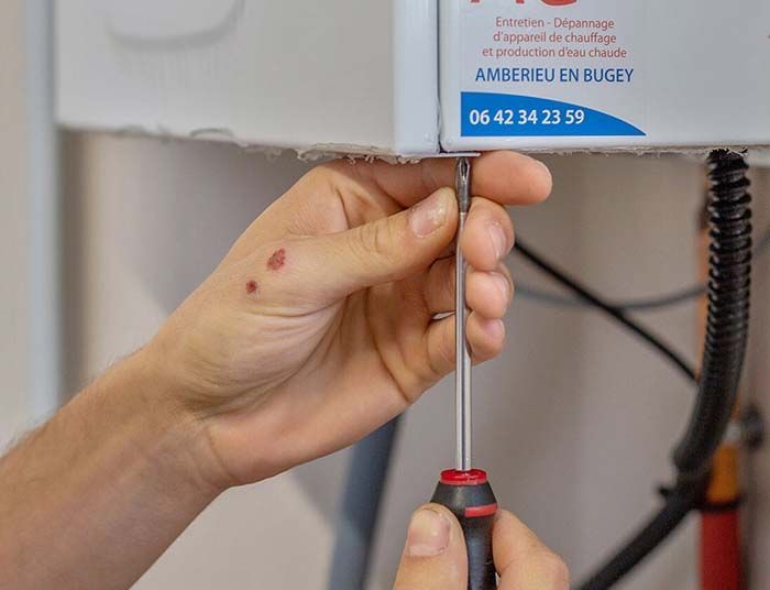 Main utilisant un tournevis pour régler la fixation. Appareil blanc, câble noir, numéro de téléphone visible.