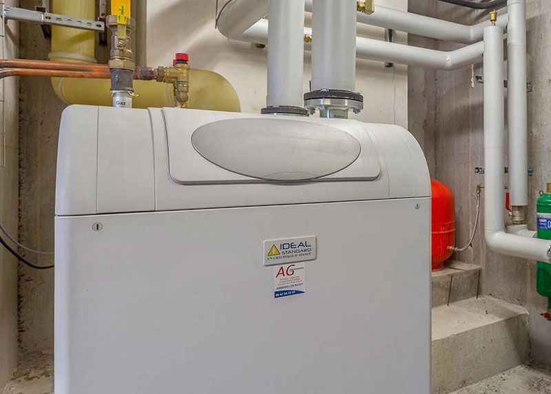 Système de chauffage blanc dans une buanderie avec tuyaux et vase d'expansion rouge.