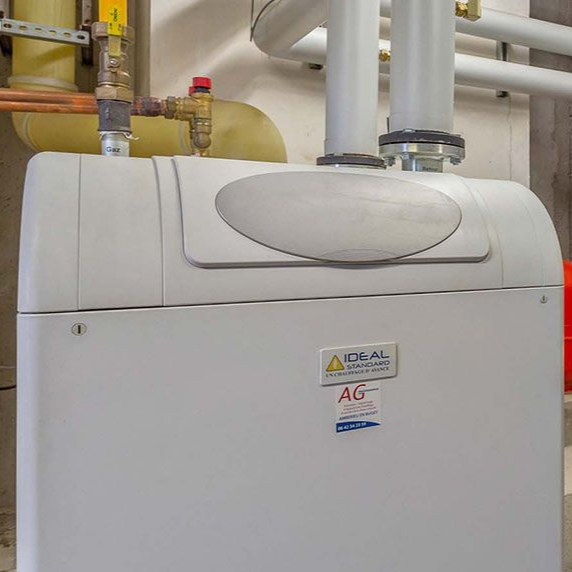 Chaudière Ideal blanche dans un local technique, tuyaux et vannes visibles.