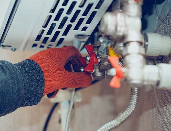 Une personne portant un gant rouge ajuste une valve rouge sur un chauffe-eau avec des tuyaux.
