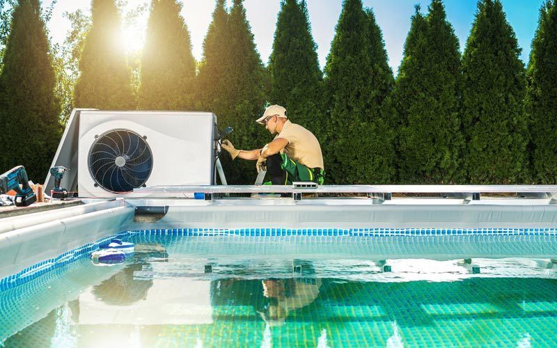 Pisciniste installant une thermopompe à côté d'une piscine. Extérieur, ensoleillé.