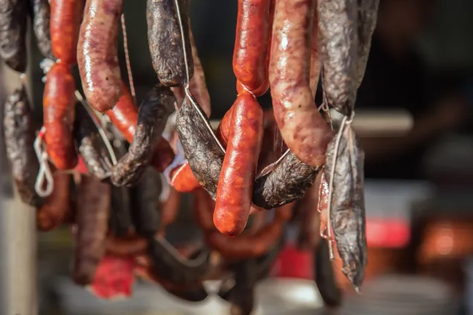 Salchichas colgadas, de varios colores desde marrón oscuro hasta rojo, atadas con hilo blanco, al aire libre.